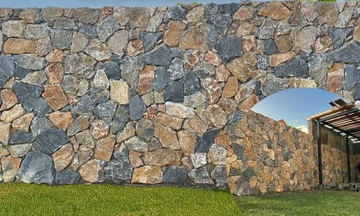 Mur en pierre sèche basaltique avec ouverture en arche sur un jardin
